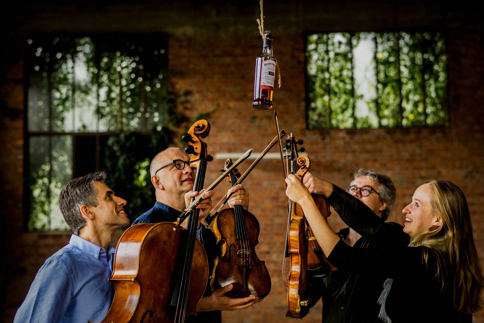 Bowmore Quartet raising their instruments beneath a hanging bottle of Bowmore whisky